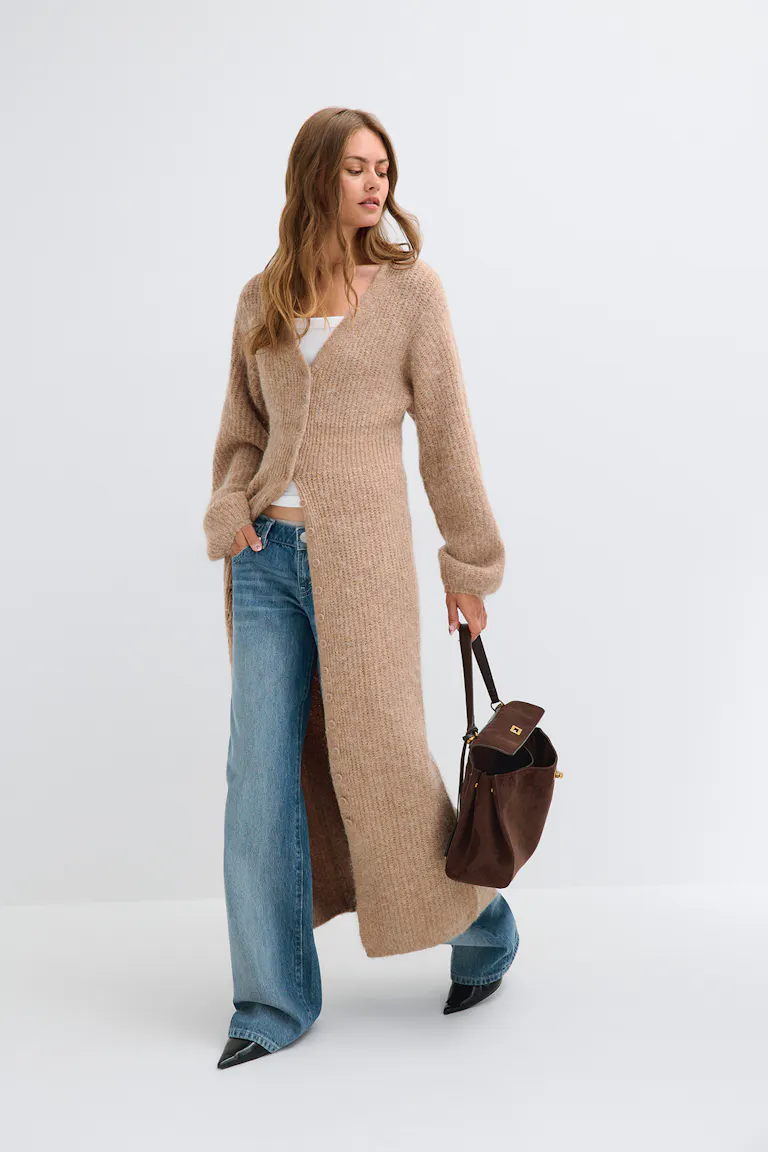 ID 319245, StyleColorSupplier 17900: Lang, beige strikket cardigan over en hvid top, blå jeans med brede ben og sorte sko med spids tå.