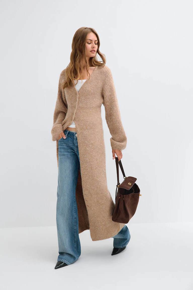 ID 319245, StyleColorSupplier 17900: Lang, beige strikket cardigan over en hvid top, blå jeans med brede ben og sorte sko med spids tå.