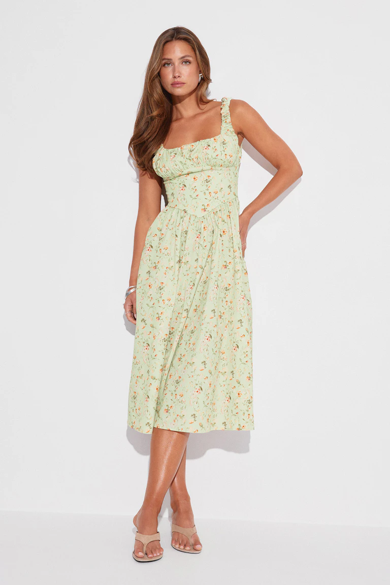 Robe midi à fleurs vert pâle avec encolure carrée froncée, bretelles volantées, taille ajustée et jupe froncée, assortie de diapositives à talons ouvertes beiges et de bracelets et boucles d'oreilles argentés.