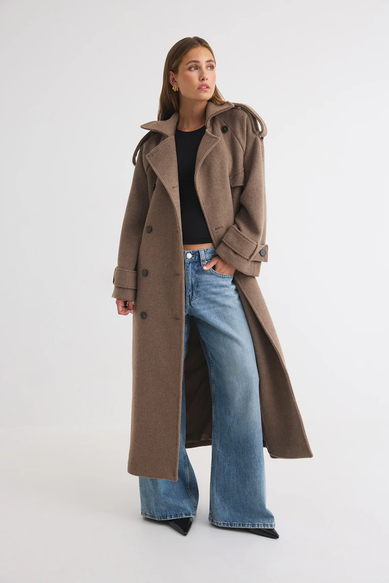 Long brown double-breasted coat over a black top, wide-leg blue jeans, and black pointed-toe shoes.