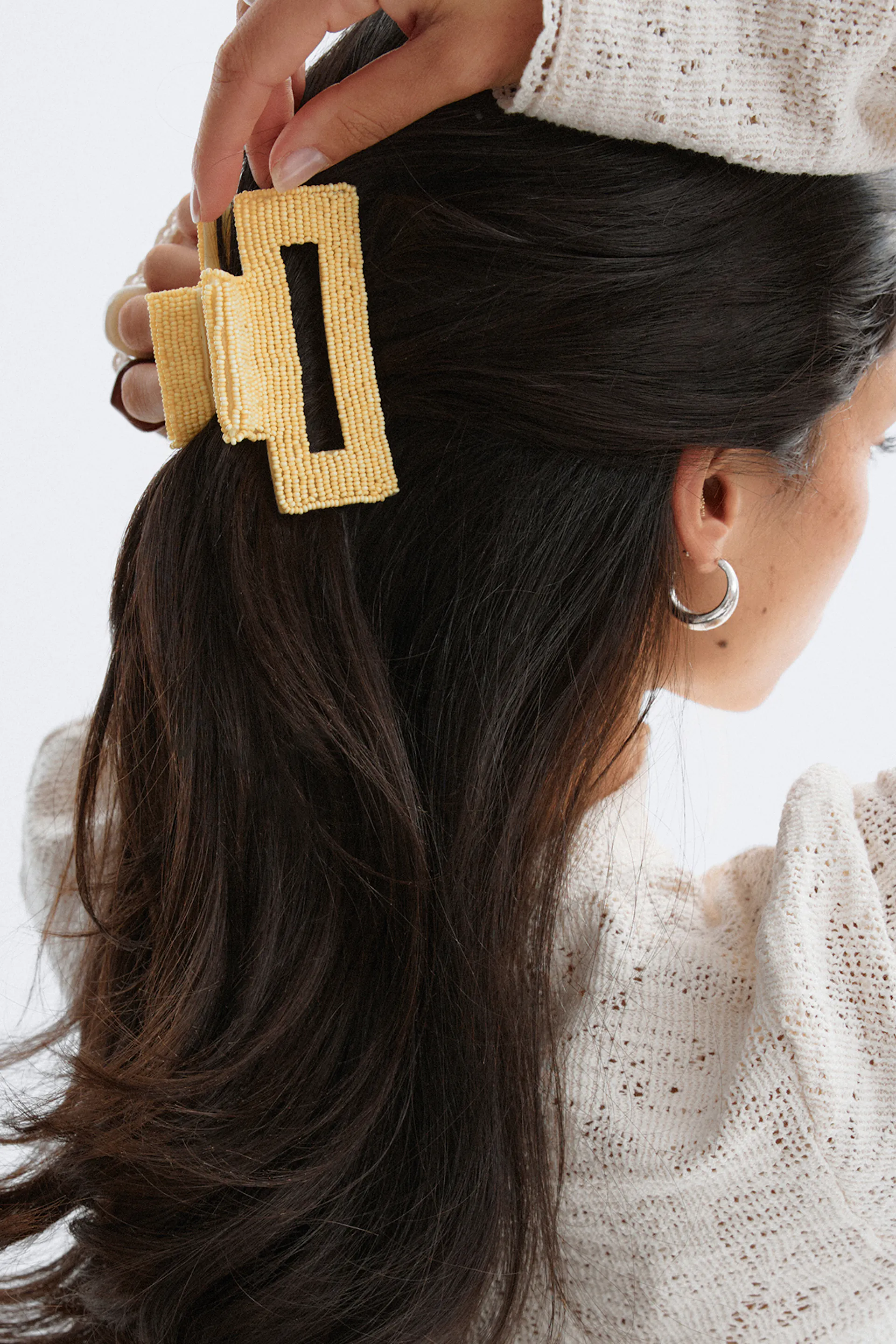 Cremefarvet åbenstrikket sweater, sølvfarvede øreringe og gul rektangulær hårklo med perler.