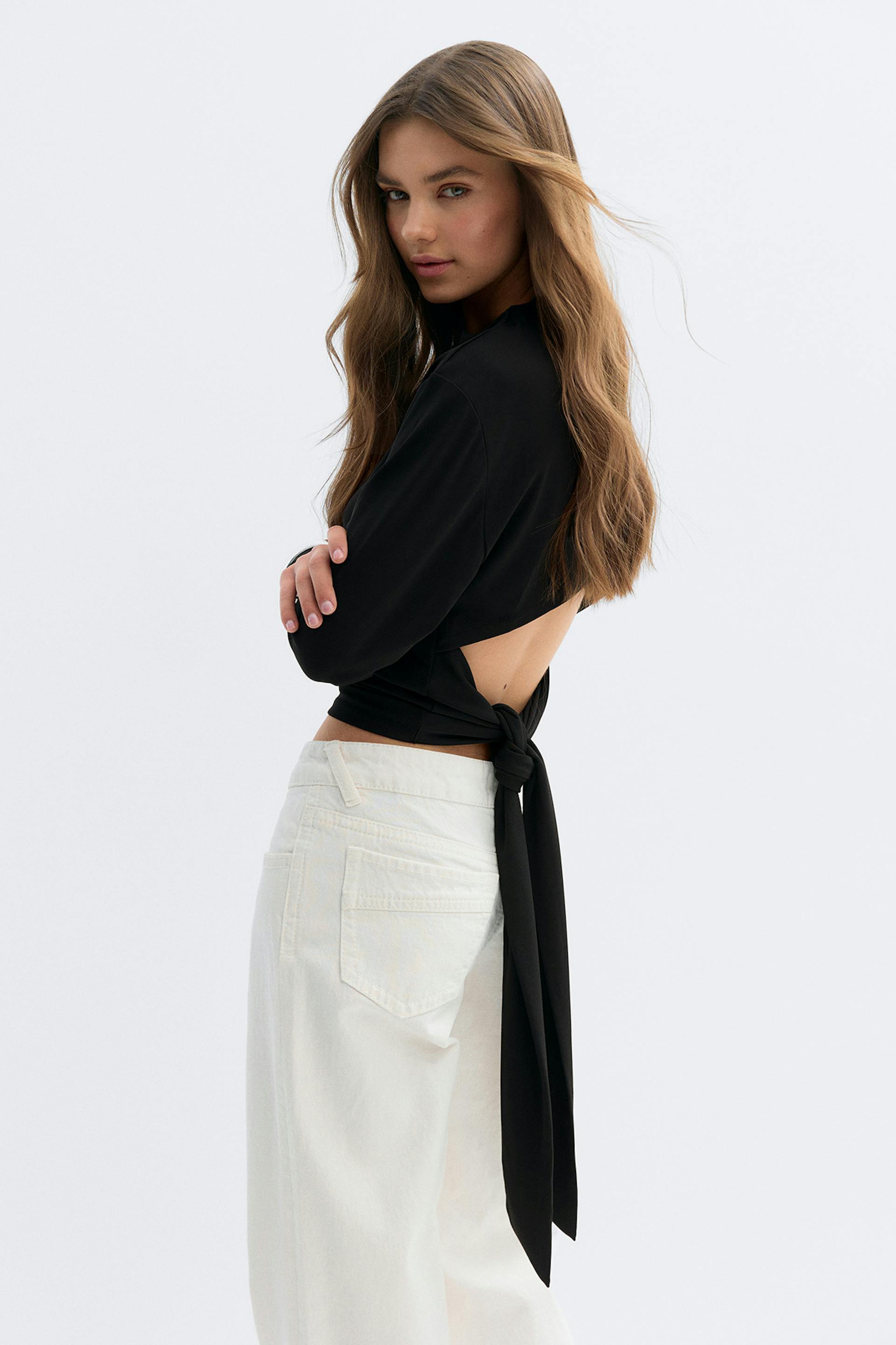 Musta pitkähihainen, pitkävartinen, avonaisella selkäosalla ja pitkällä solmitulla vyöllä varustettu yläosa, joka on yhdistetty korkeavyötäröisiin valkoisiin leveälahkeisiin farkkuihin.