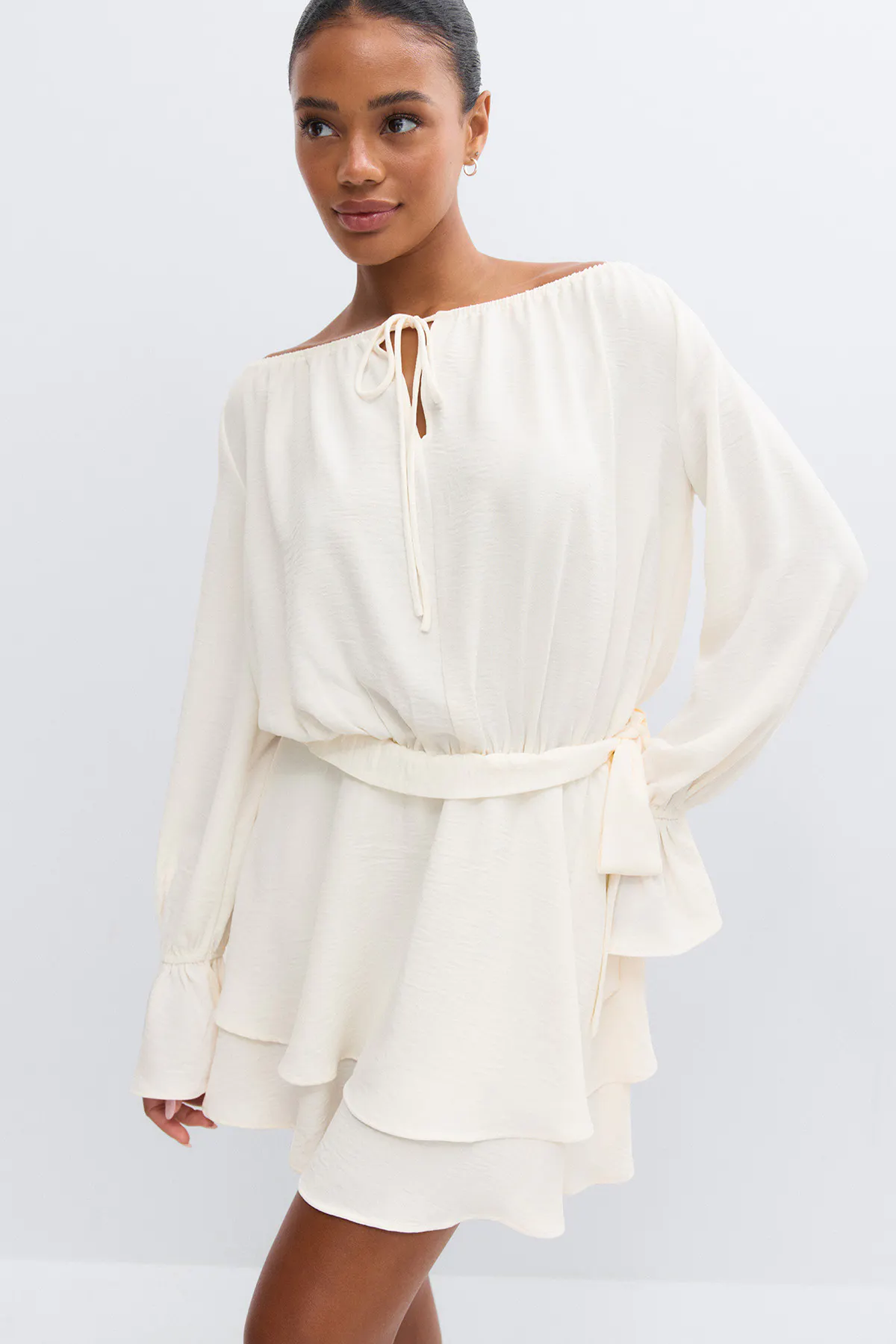 Cremefarbenes, schulterfreies, langärmeliges Kleid mit gebundenem Ausschnitt, elastischer Taille mit passendem Stoffgürtel und gestuftem, gerüschtem Rockteil.