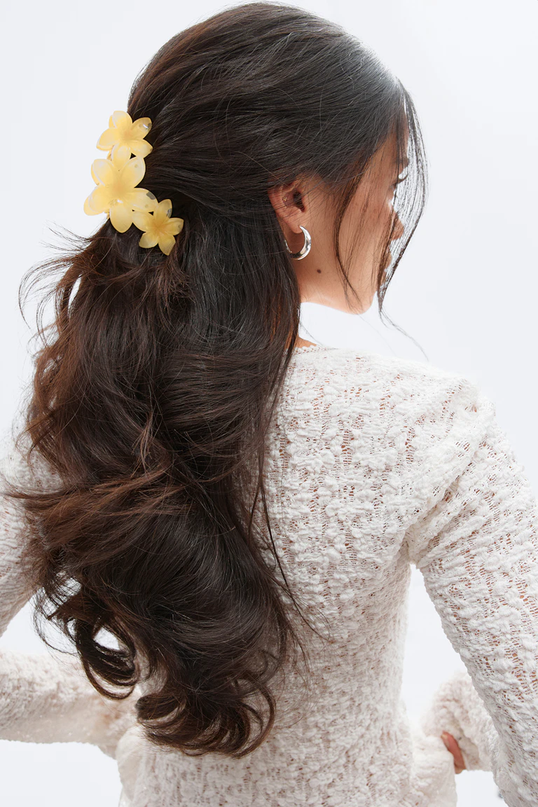 Weißes, strukturiertes, langärmeliges Strickoberteil, silberne Ohrringe und eine gelbe Haarspange mit drei Blumen.