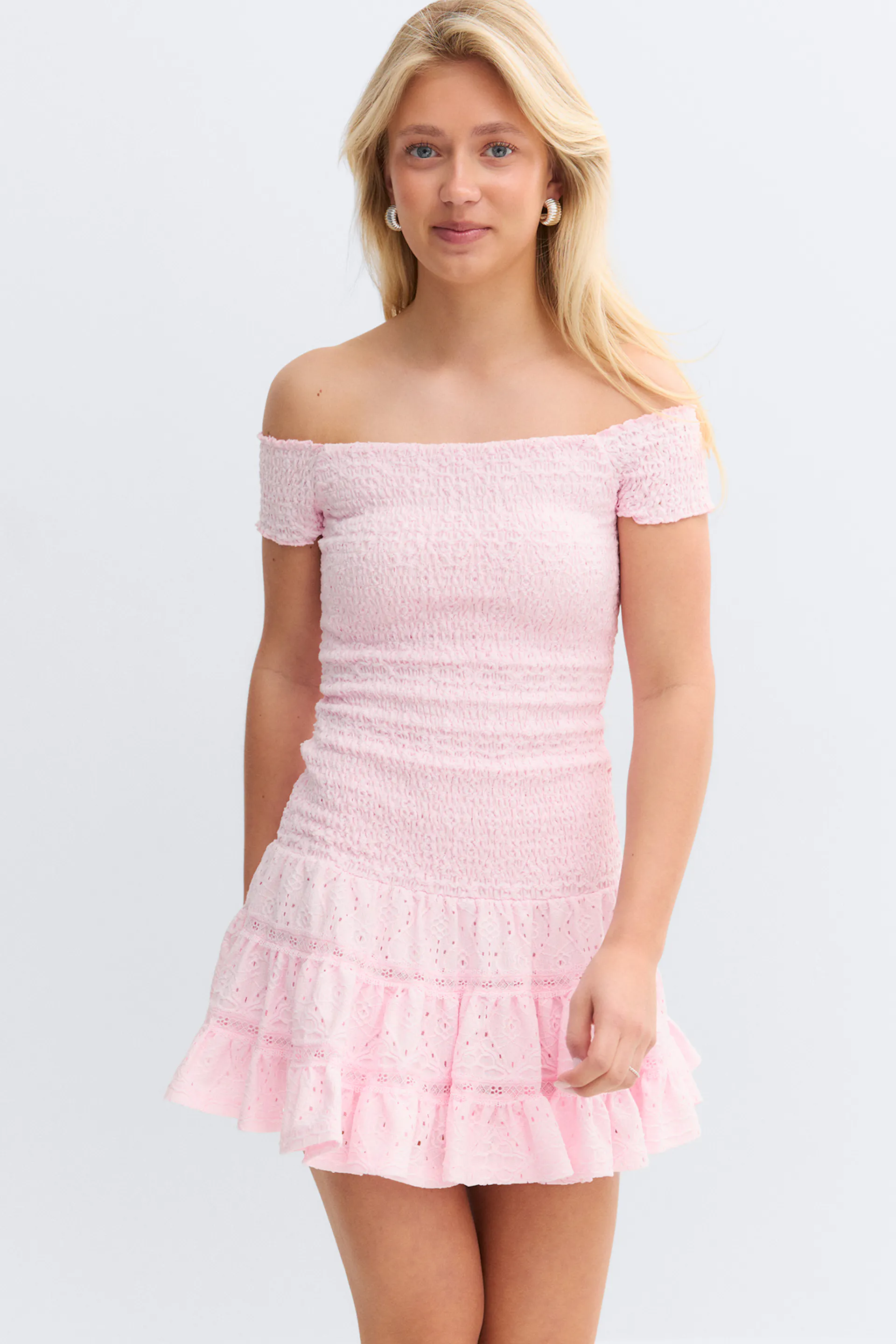 Mini robe rose pâle à épaules nues avec un corsage smocké, des manches courtes et une jupe à volants en œillets.
