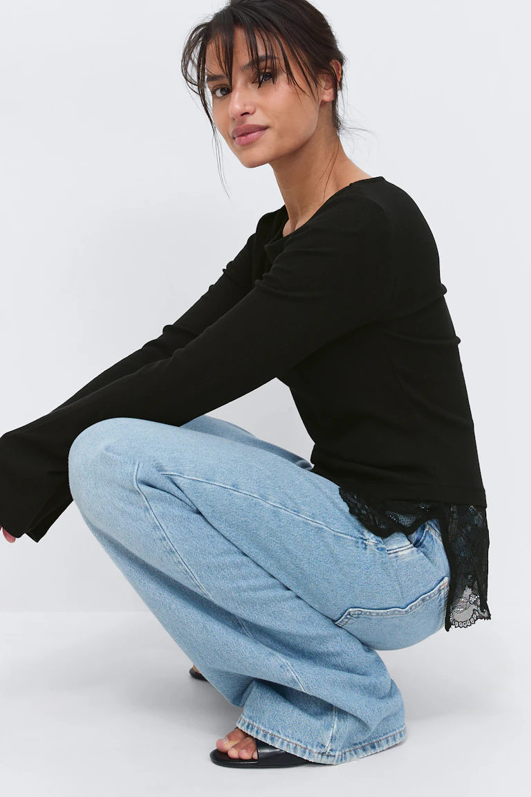 Sort langærmet ribbet top med blondekant forneden, lysvaskede jeans med brede ben og sorte slidesandaler med åben tå.