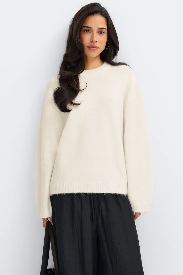 Cremefarbener Strickpullover mit Rundhalsausschnitt, gerippten Bündchen und Saum, kombiniert mit einer lockeren schwarzen Hose mit weitem Bein.
