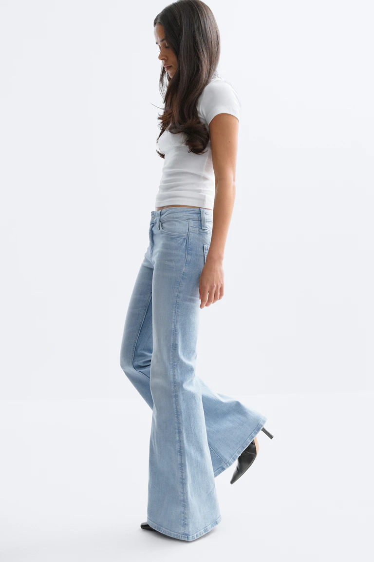 Fitted white short-sleeve crop top, light‑wash high‑rise flared jeans, and black pointed‑toe heeled mules.