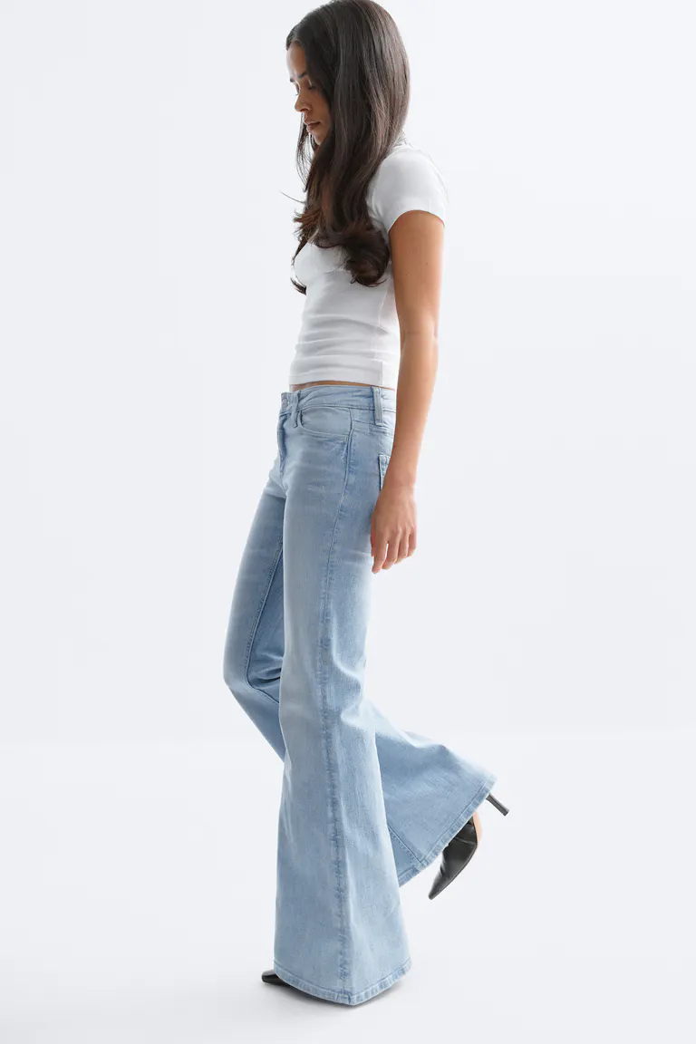 Fitted white short-sleeve crop top, light‑wash high‑rise flared jeans, and black pointed‑toe heeled mules.
