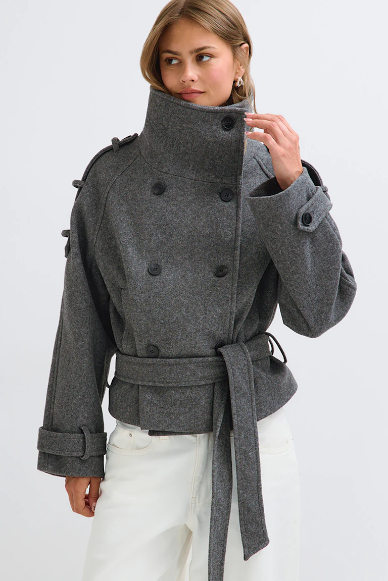ID 320311, StyleColorSupplier 16657: Das Model trägt eine graue Jacke mit hohem Kragen, Gürtel, doppelreihiger Knopfleiste und Manschettenriemen, dazu eine weiße Hose.