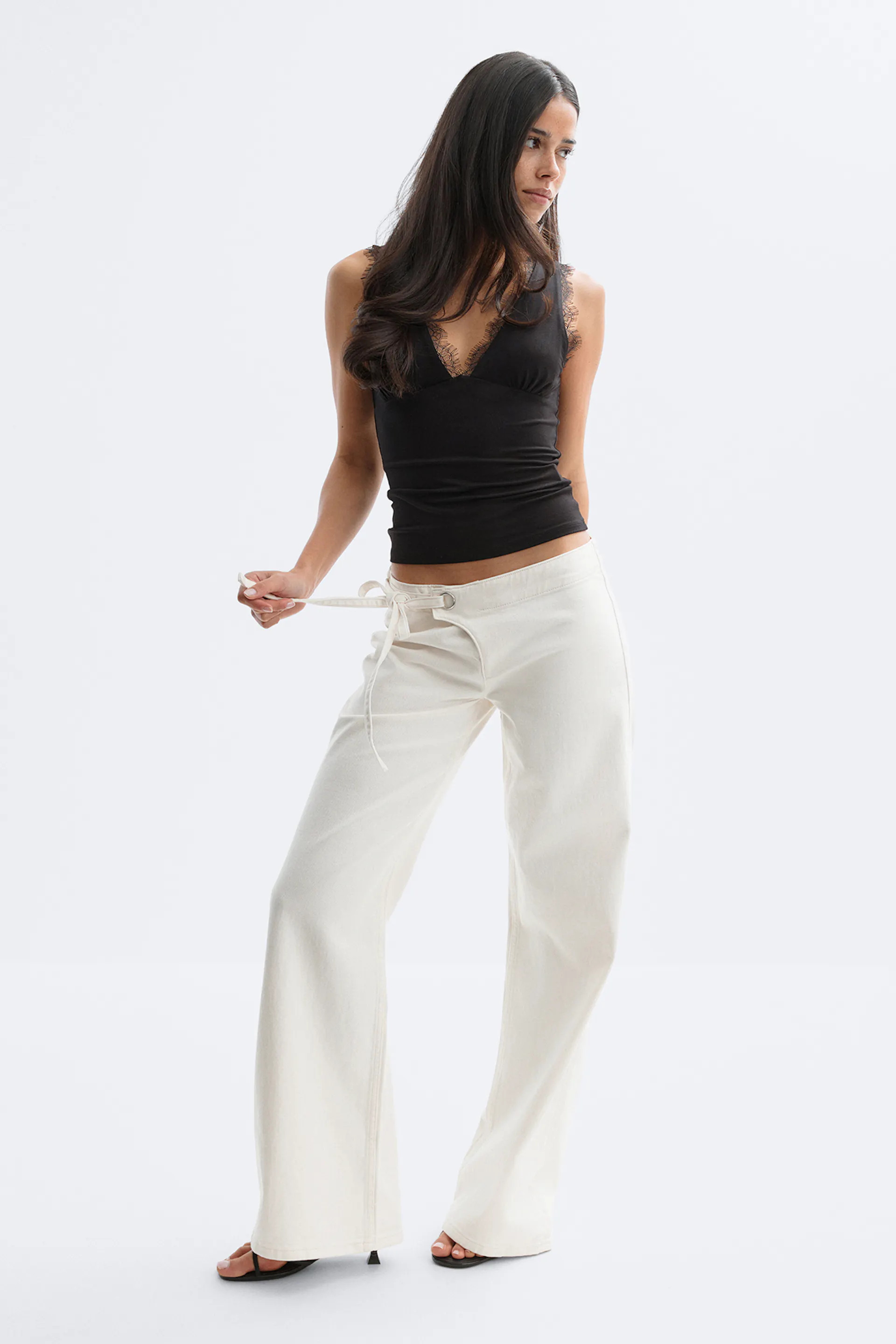 Sort camisole med V-udskæring og blonder sammen med cremefarvede bukser med vidde og snøre og sorte sandaler med åben hæl.