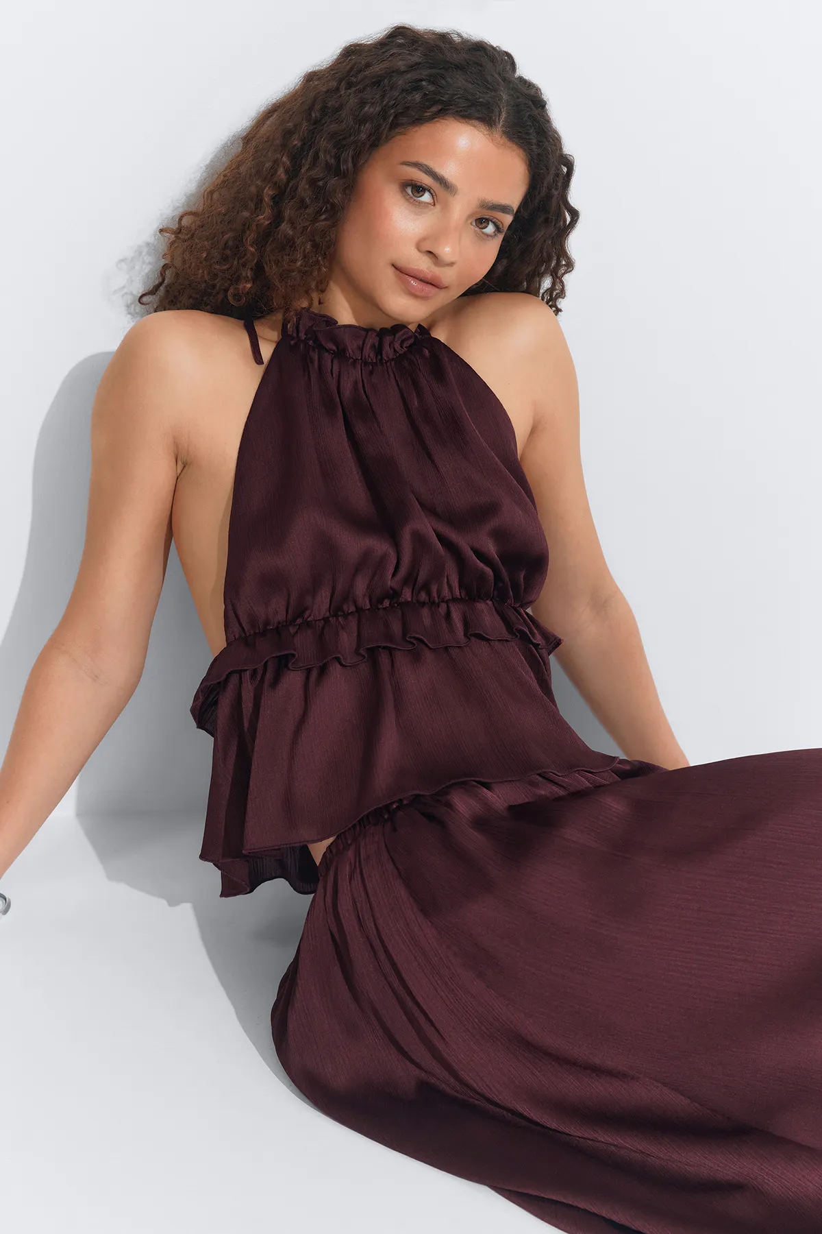 Top licou en satin bourgogne avec encolure froncée et détails à volants, associé à une jupe longue fluide assortie.