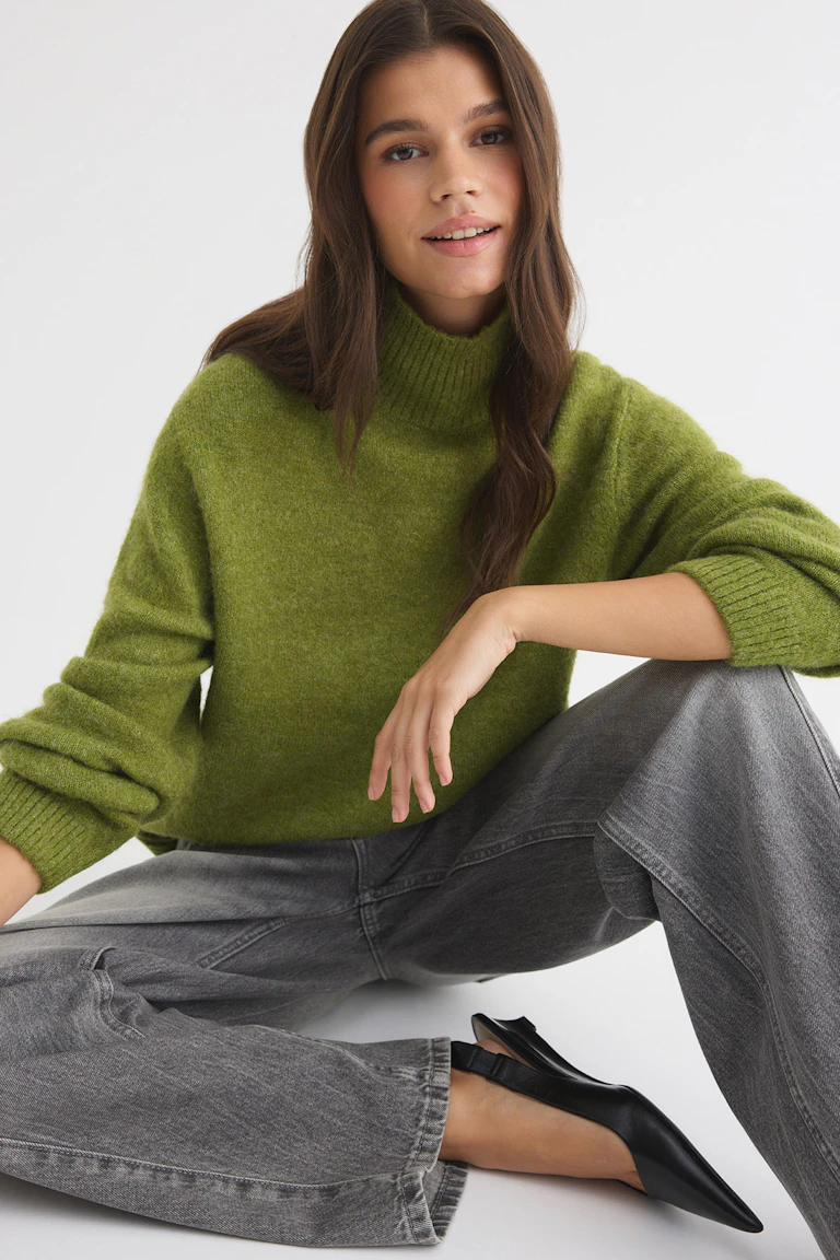 Grüner Rollkragenpullover, graue Jeans mit weitem Bein und schwarze spitze Slingback-Ballerinas.