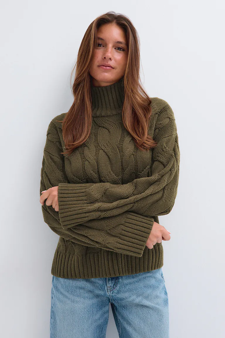 Olivgrüner Rollkragenpullover im Zopfmuster zu hellblauen Jeans.