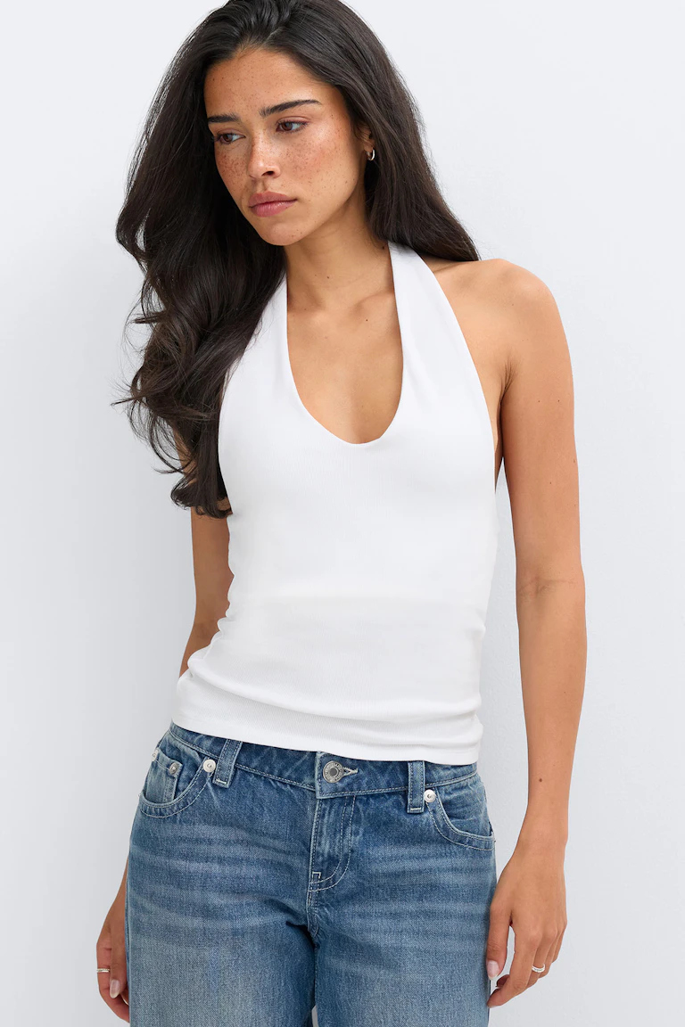 Weißes, geripptes Neckholder-Top mit tiefem Rundhalsausschnitt, kombiniert mit mittelblauen Jeans mit hoher Taille.