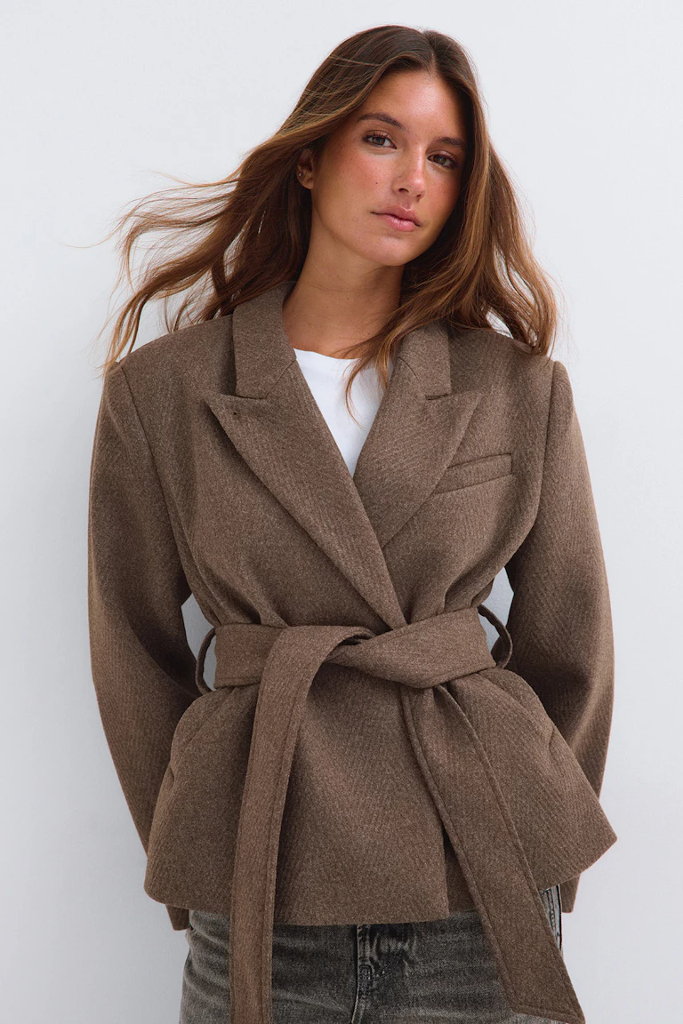 Brown belted blazer over a white top, paired with dark jeans.
