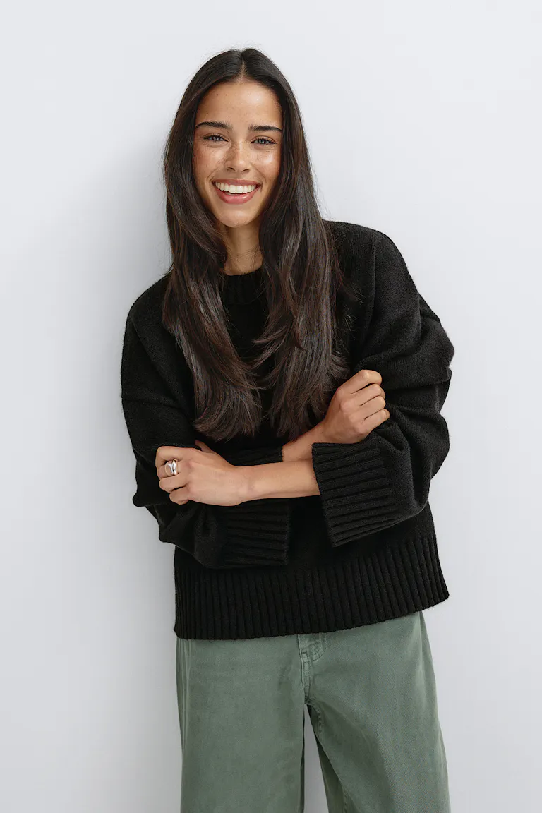 Schwarzer, übergroßer Strickpullover mit gerippten Bündchen und Saum, kombiniert mit einer olivgrünen Hose mit weitem Bein und einem silbernen Ring.