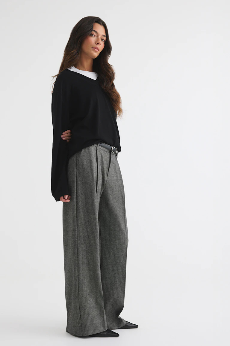 id: 333348  
StyleColorSupplier: 16657  
Black oversized V-neck sweater layered over a white top, paired with wide-leg grey trousers, a black belt, and black pointed shoes.