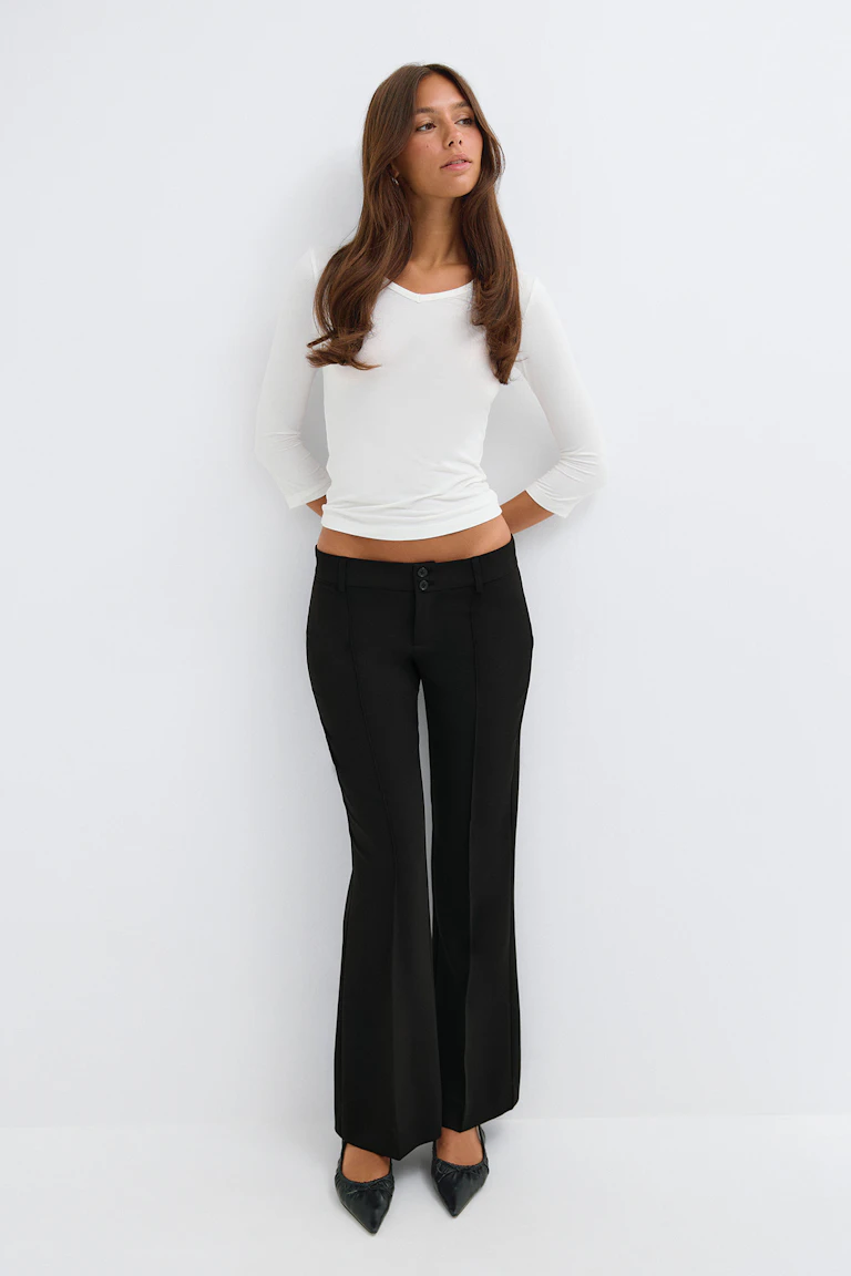 Un haut blanc ajusté à manches trois-quarts, associé à un pantalon noir évasé à taille haute et à des ballerines noires à bout pointu.