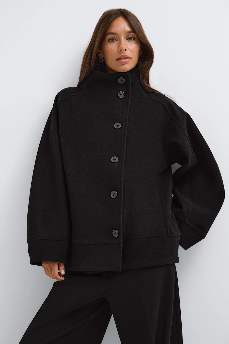 Black high-neck button-front jacket with wide sleeves and matching wide-leg trousers.