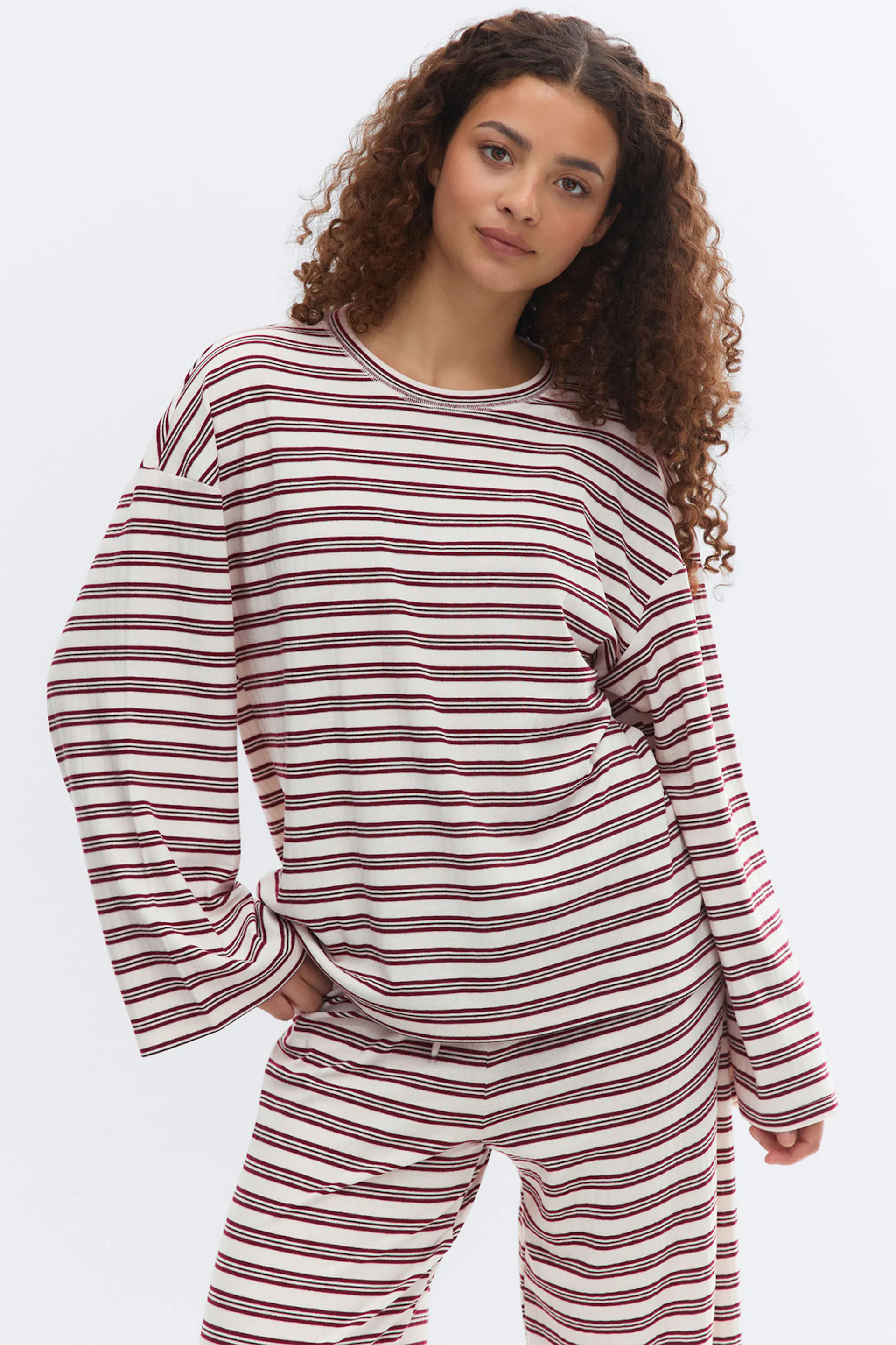 Top oversize à col ras du cou et manches longues en crème avec de fines rayures horizontales bordeaux et noires, associé à un pantalon rayé de coupe décontractée assorti.