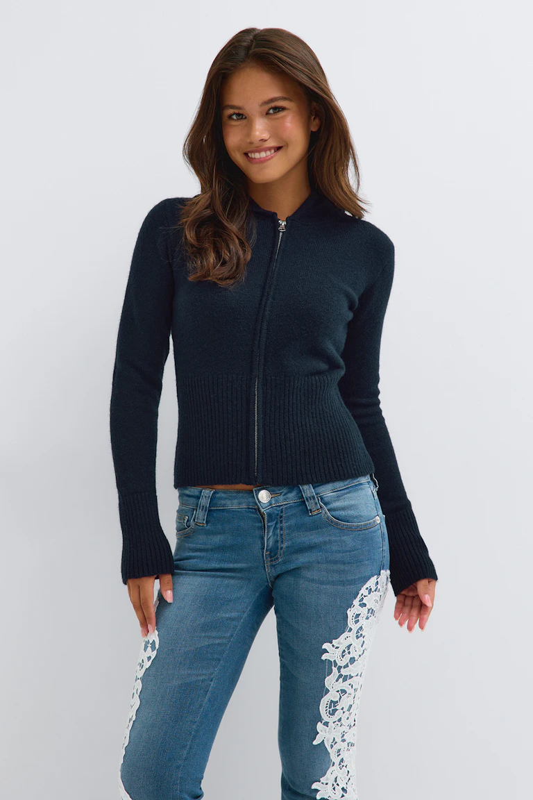 Marineblaue Strickjacke mit Reißverschluss vorne, kombiniert mit blauen Jeans und weißer Spitzenapplikation.