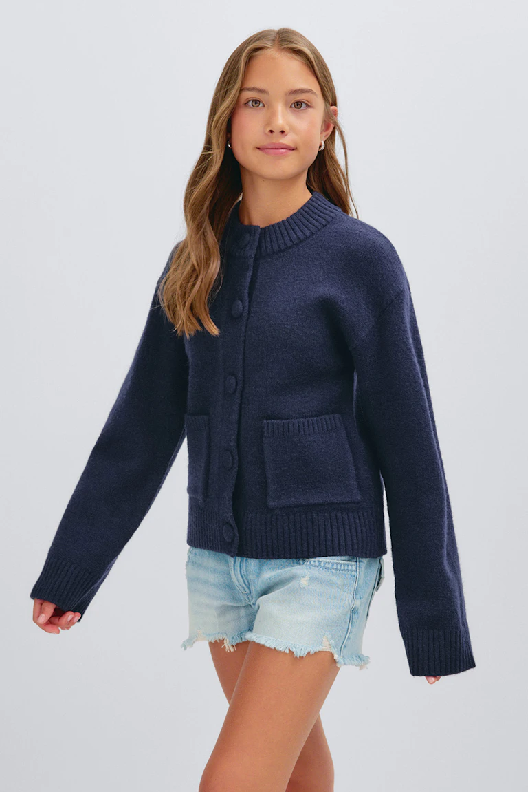 Marineblaue Strickjacke mit Knopfleiste, geripptem Kragen, Ärmelbündchen und Saum sowie aufgesetzten Taschen auf der Vorderseite, gepaart mit hellen Jeans-Shorts im Used-Look.