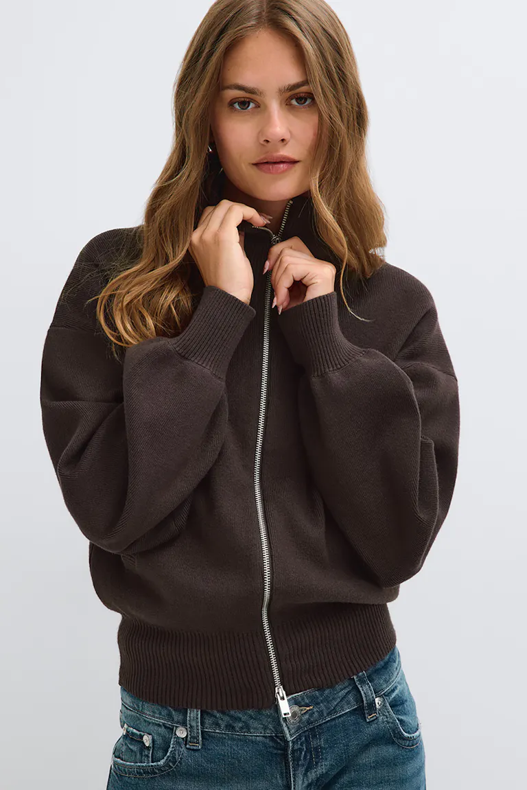 Mørkebrun sweater med lynlås og ribkant, kombineret med blå jeans.