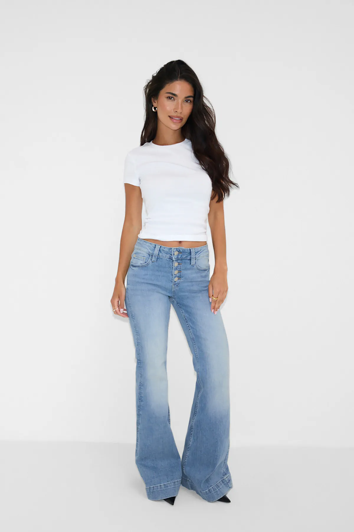 Vit kortärmad T-shirt med rund halsringning, ljus tvättade jeans med hög resår och knappslå, svarta spetsiga klackar och örhängen i guld med guldringar.