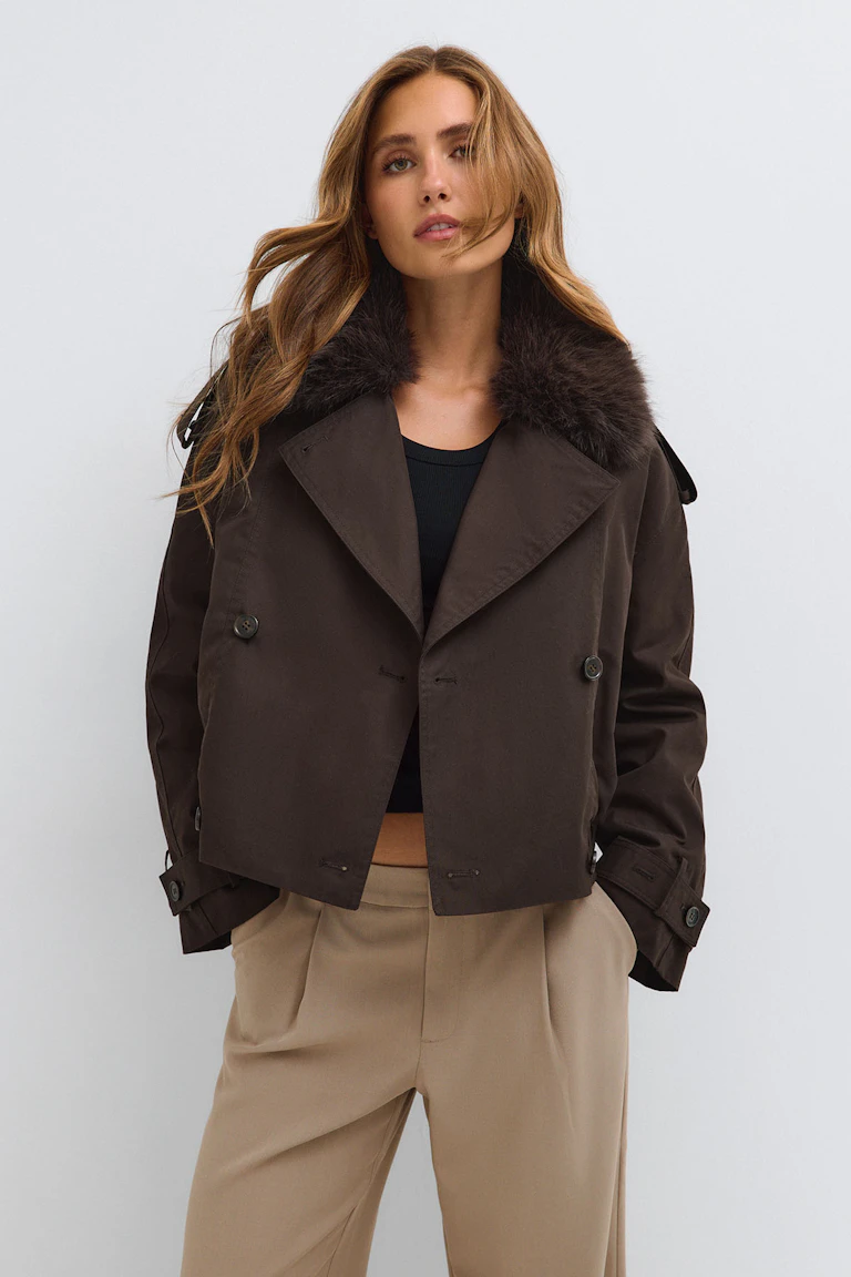 En mörkbrun kort rock med krage av fuskpäls, som bärs över en svart topp och beige byxor.