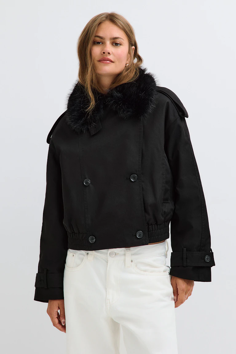 Schwarze, kurz geschnittene Jacke mit Kunstfellkragen und weiße Jeans.