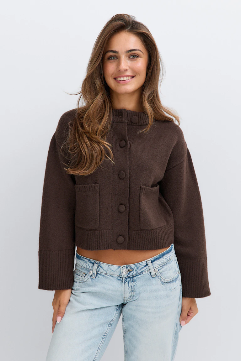 Kort, mørkebrun strikket cardigan med knapper foran, ribbestrikket krage, nederkant og mansjetter samt to påsydde lommer foran, kombinert med høyt sittende, avslappede jeans i lys vask.