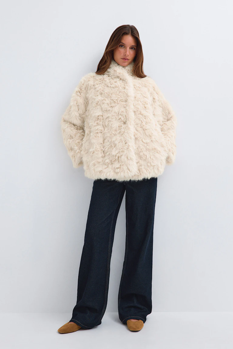 En krämfärgad jacka i fuskpäls, mörka jeans med vida ben och beige spetsiga ballerinaskor.