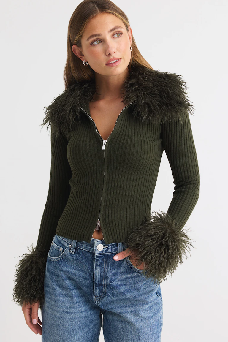 ID 326697, StyleColorSupplier 12006: Dunkelgrünes, geripptes Oberteil mit Reißverschluss vorne und Kunstfellbesatz, kombiniert mit einer blauen Jeans.