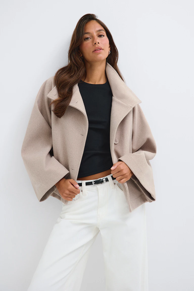 Ein übergroßer Mantel in Blush über einem schwarzen Oberteil, kombiniert mit einer weißen Hose und einem schwarzen Gürtel.