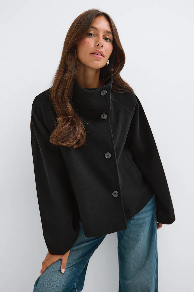 Schwarze Jacke mit Knöpfen und weiten Ärmeln sowie blaue Jeans.