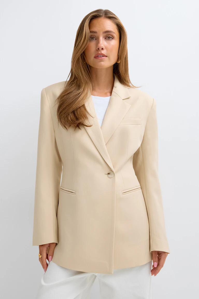 Beige tailored blazer over a white top and white trousers.