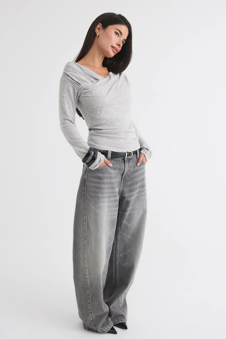 En ljusgrå, draperad långärmad topp tillsammans med grå jeans med vida ben, ett svart bälte och svarta spetsiga skor.