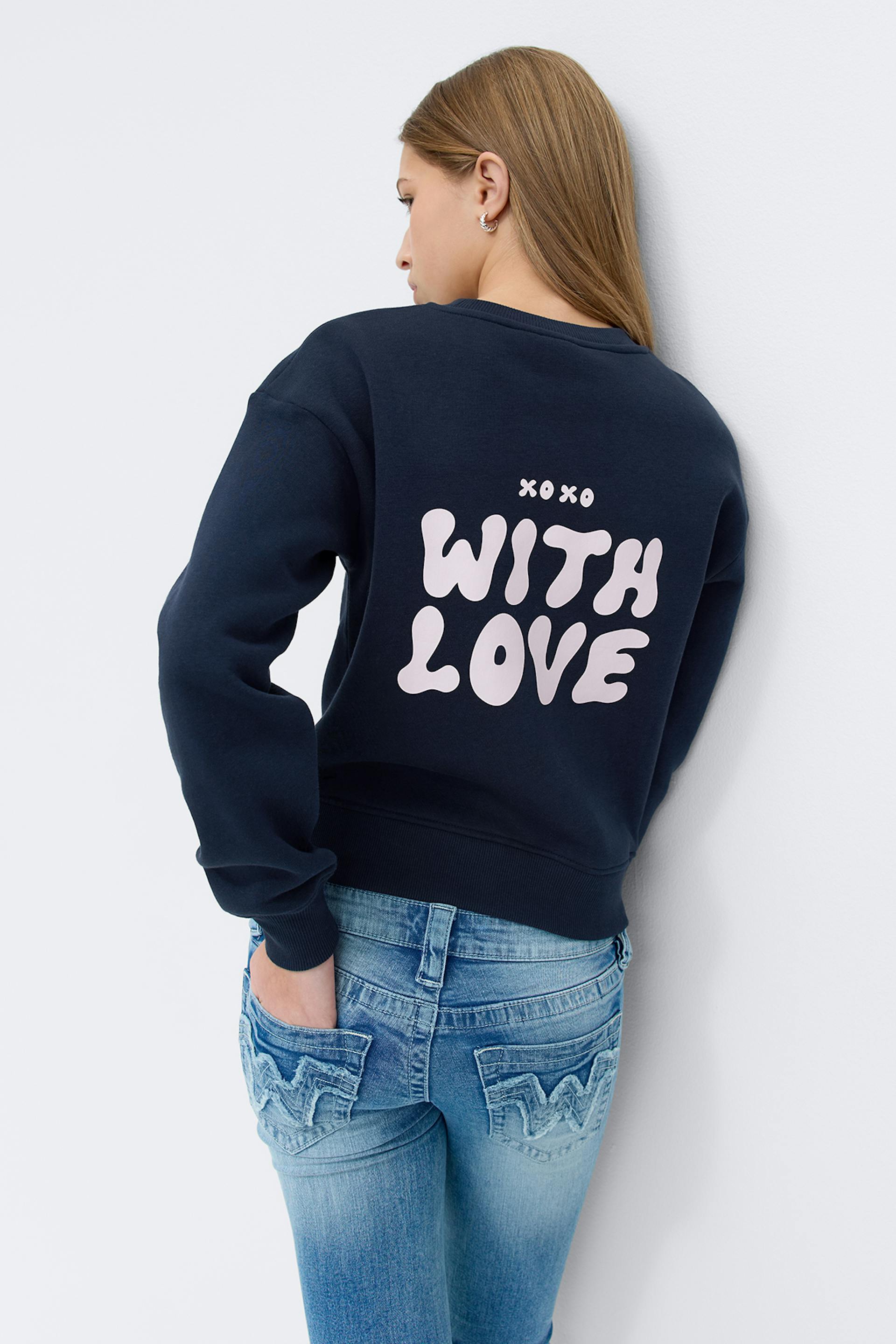 Laivastonsininen collegepaita, jossa vaaleanpunainen "WITH LOVE" -selkäpainatus, yhdistettynä vaalean sinisiin farkkuihin, joissa on kirjaillut takataskut.