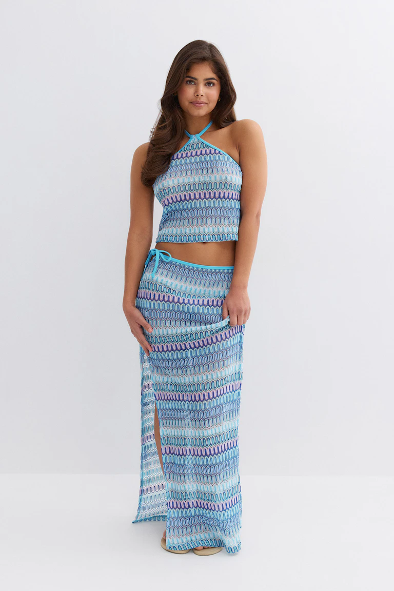 Sleeveless halter-neck cropped top paired with a matching long drawstring skirt featuring a side slit, both in a blue multicolored wavy geometric print with turquoise trim.