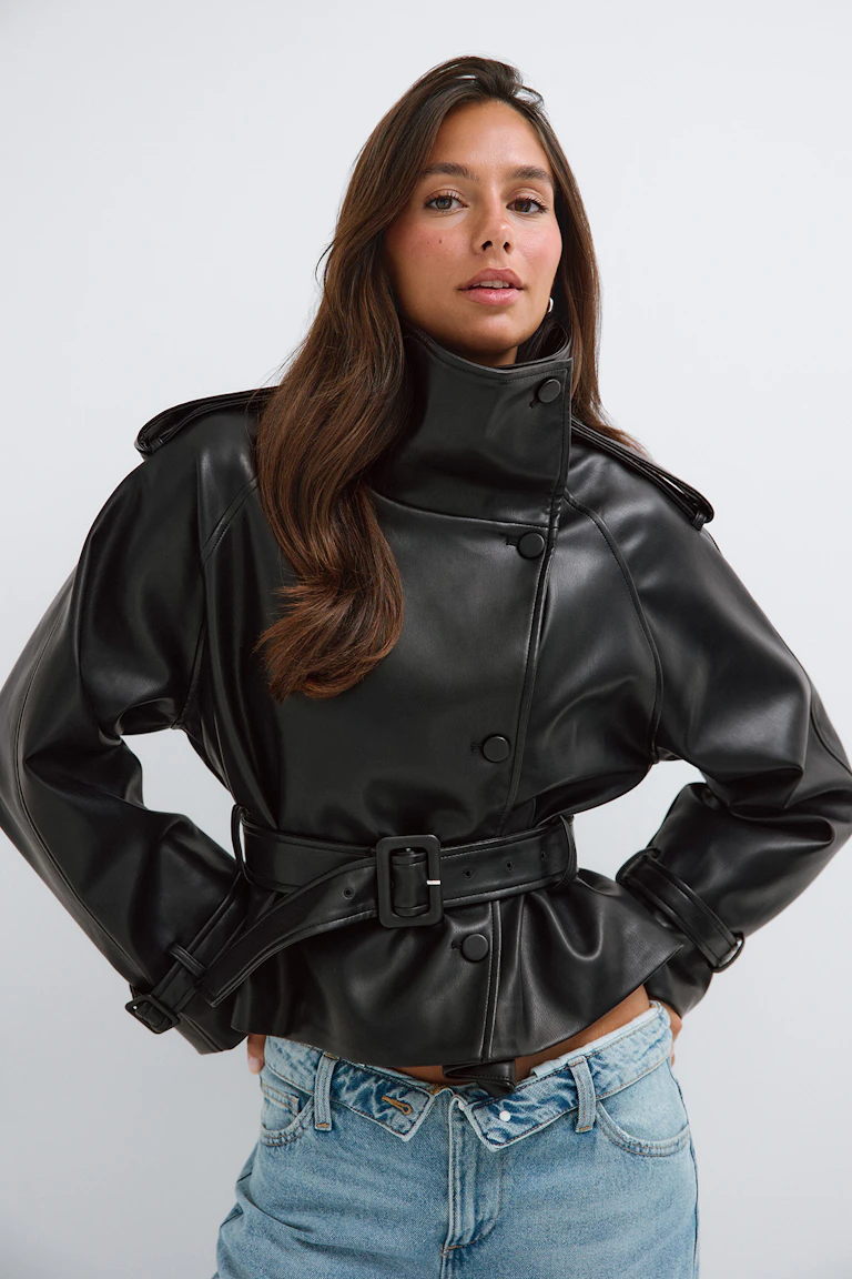 Black belted faux-leather jacket with a high collar, paired with light blue jeans.