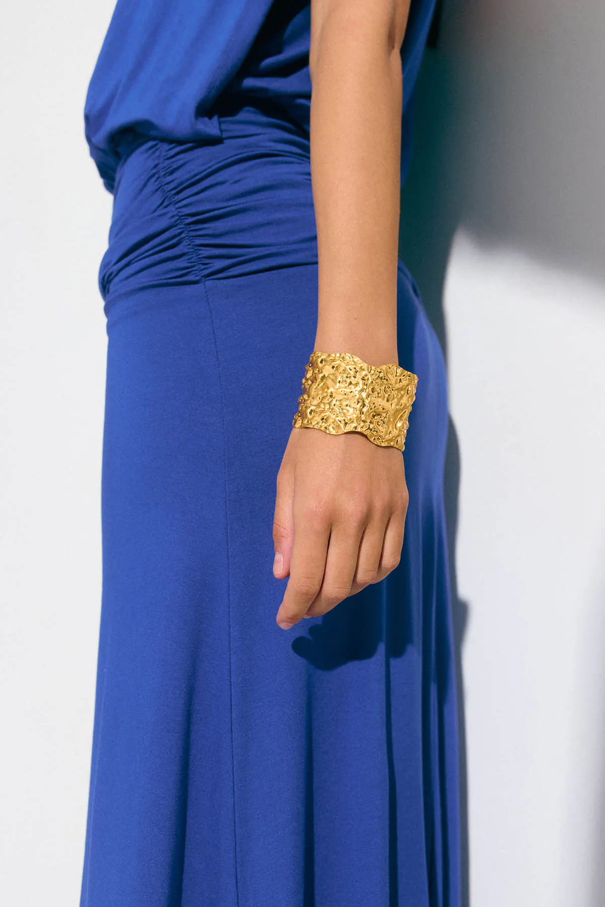 Ärmelloses kobaltblaues Rüschenkleid mit langem Rock, gepaart mit einem breiten, strukturierten Goldarmband.