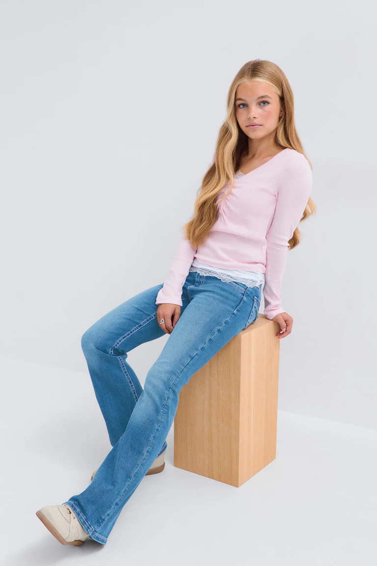Ein hellrosa Langarm-Oberteil zu einer blauen Schlagjeans und cremefarbenen Sneakern.