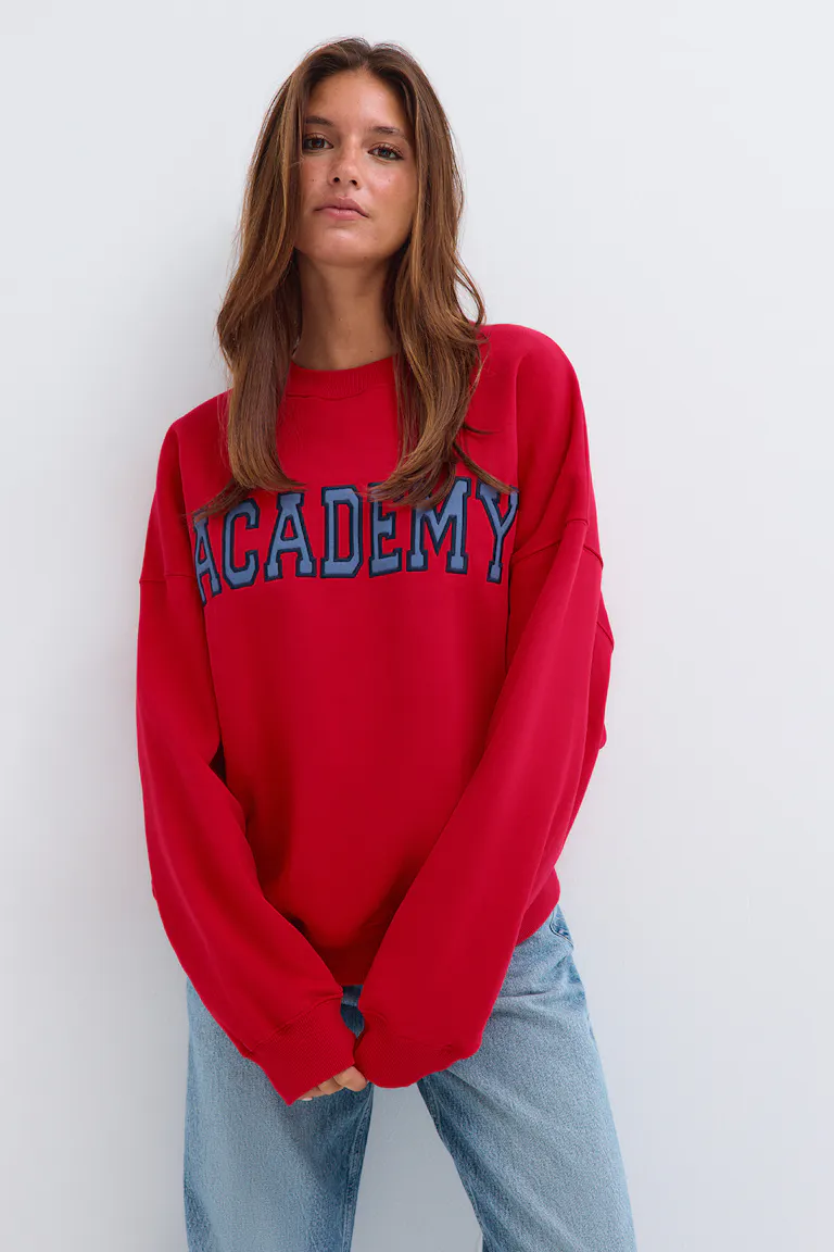 ID 345422 | StyleColorSupplier 11519-E : Sweat-shirt oversize rouge avec l'inscription « ACADEMY » et un jean bleu clair.
