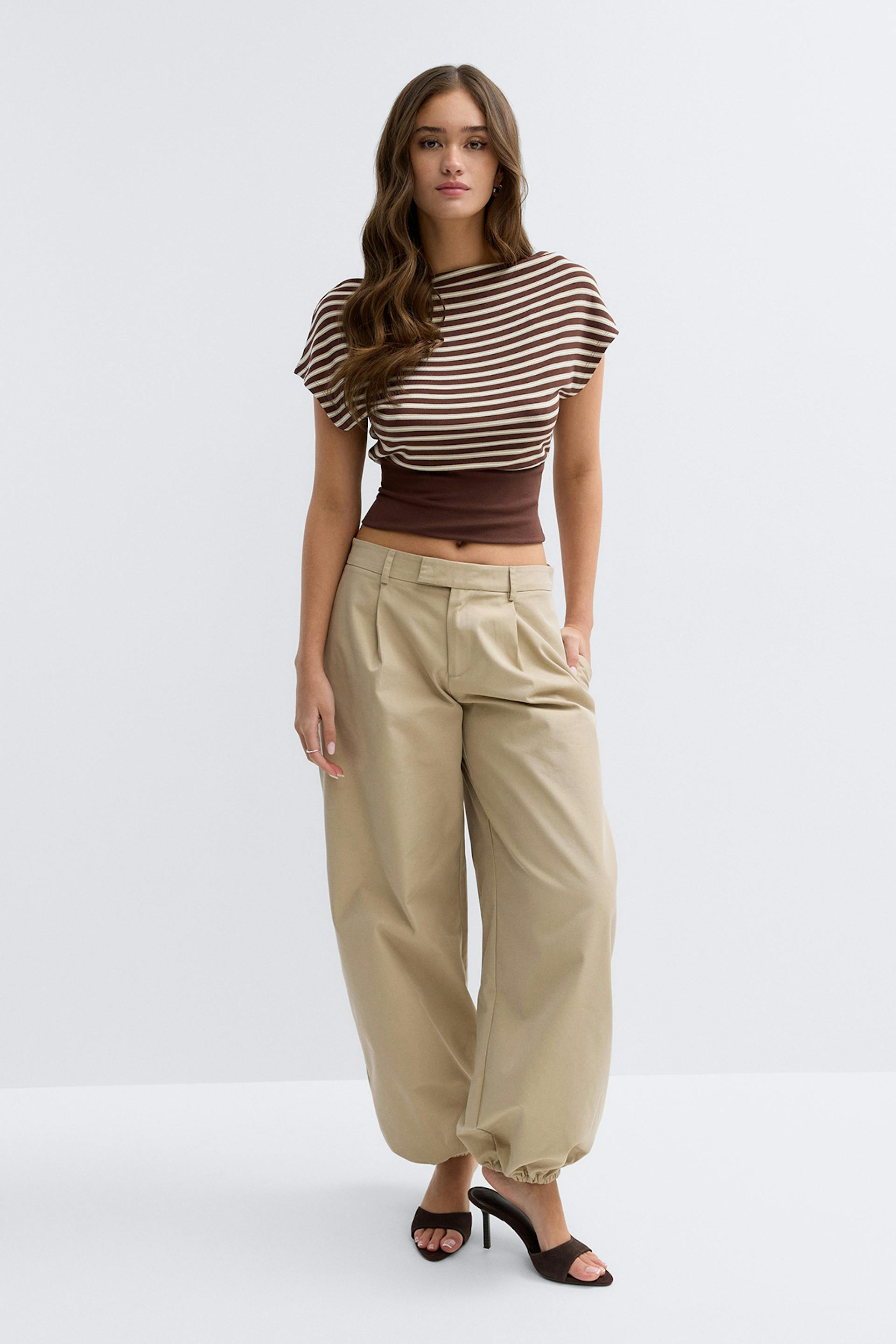 Braun-cremefarbenes, horizontal gestreiftes, kurzärmeliges Oberteil mit dunkelbraunem Tailleneinsatz, beigefarbene Hose mit weitem Bein und elastischem Saum sowie dunkelbraune Pantoletten mit offenen Zehen.