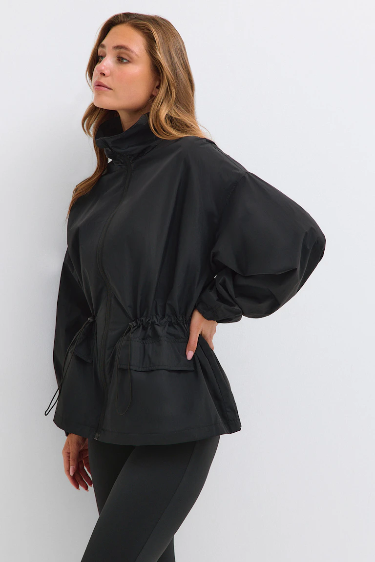Schwarze Windjacke mit hohem Kragen, tailliertem Schnitt und schwarzen Leggings.