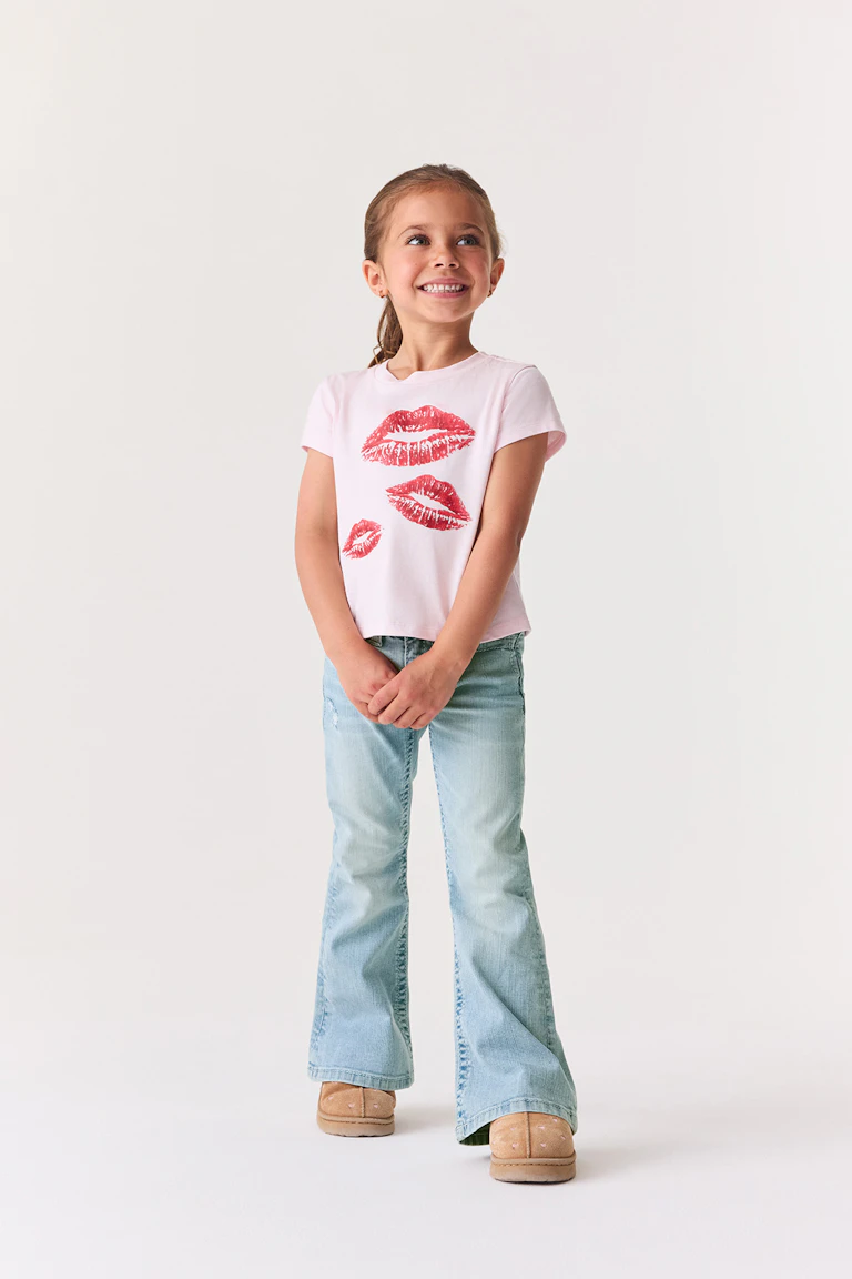 Lyserød T-shirt med rødt læbe-print, lyseblå jeans med udvidede ben og beige slip-on-sko.