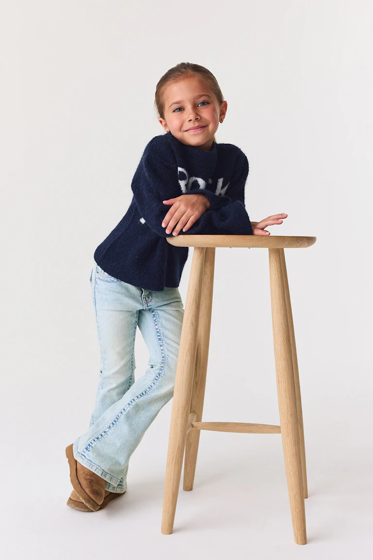 En marineblå, lodden sweater med hvid skrift, lysvaskede jeans med udvidede ben og lysebrune ruskindsstøvler.