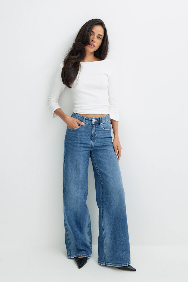Vit långärmad tröja och blå jeans med vida ben.