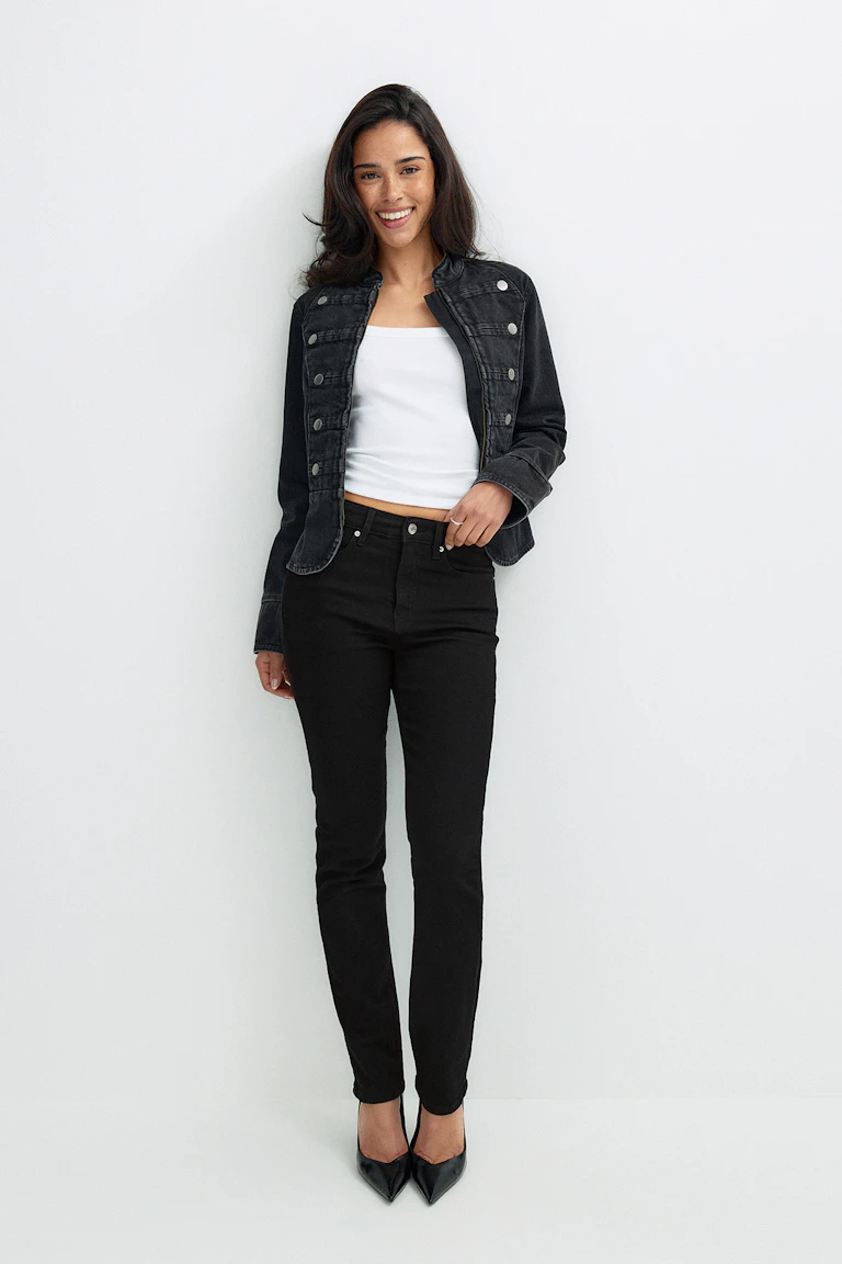 Schwarze Jacke, weißes Oberteil, schwarze Jeans und schwarze Pumps.